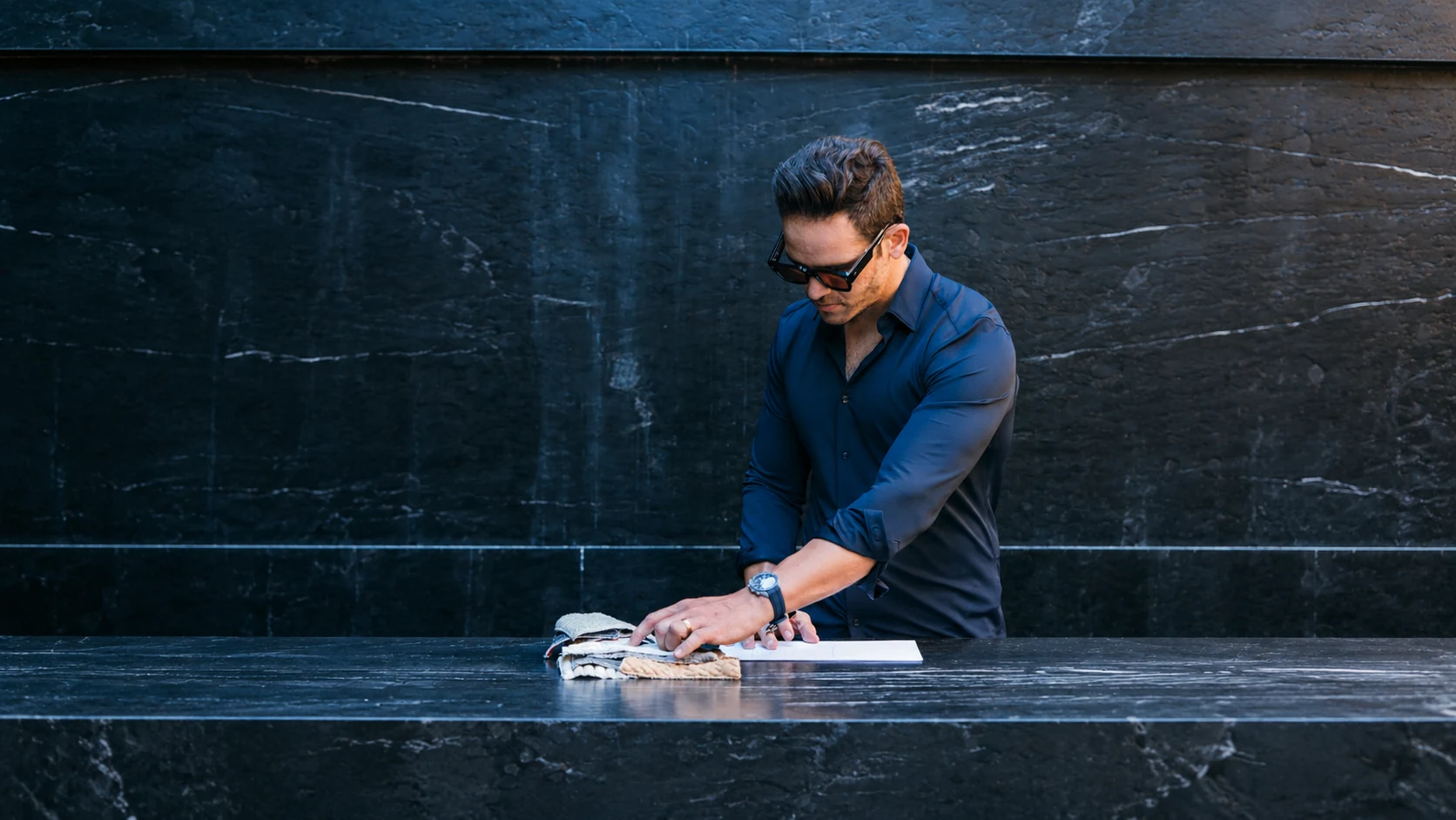 Designer André Gurgel working with textile samples at a black stone table